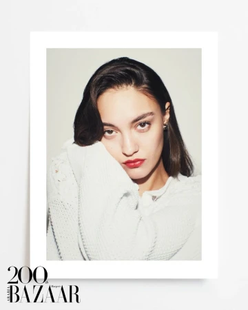 Portrait of a model wearing a white knit cardigan with bold red lipstick against a plain white studio background.