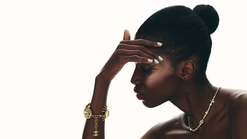Close-up profile of a black woman wearing gold jewelry and a pendant necklace against a white background