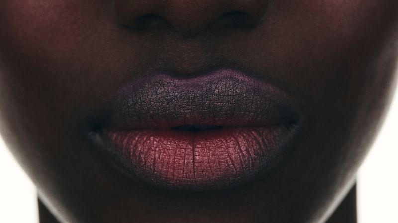 Close-up on an adult female face, highlighting lips adorned with dark red and purple lipstick in a beauty and fashion context.