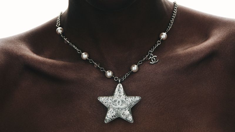 Necklace featuring a star pendant on a woman's dark skin, emphasizing jewelry, pearls, and metal accents in a close-up fashion shot.