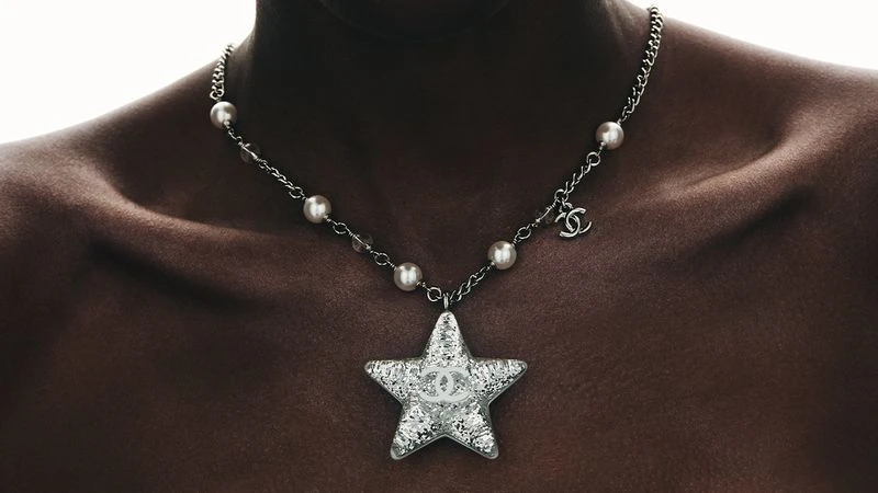 Necklace featuring a star pendant on a woman's dark skin, emphasizing jewelry, pearls, and metal accents in a close-up fashion shot.