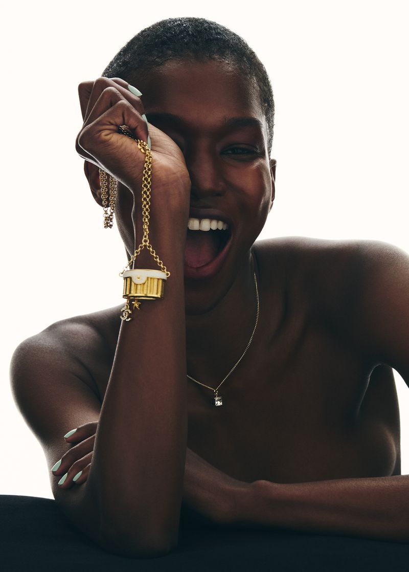 Striking close-up of a happy Black female model wearing a gold charm necklace. Beauty and fashion photography with soft studio lighting.