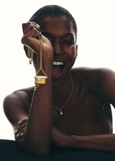 Striking close-up of a happy Black female model wearing a gold charm necklace. Beauty and fashion photography with soft studio lighting.