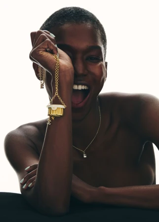 Striking close-up of a happy Black female model wearing a gold charm necklace. Beauty and fashion photography with soft studio lighting.