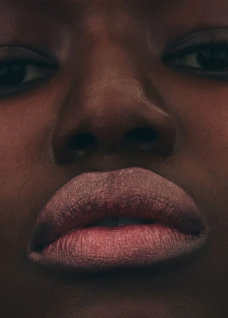 Close-up portrait of an adult woman with dark skin, showcasing her facial features, specifically her eyes, nose, and lips.