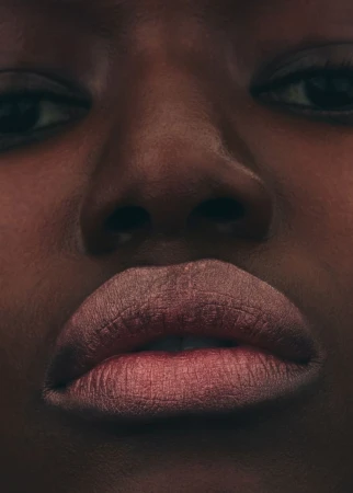 Close-up portrait of an adult woman with dark skin, showcasing her facial features, specifically her eyes, nose, and lips.