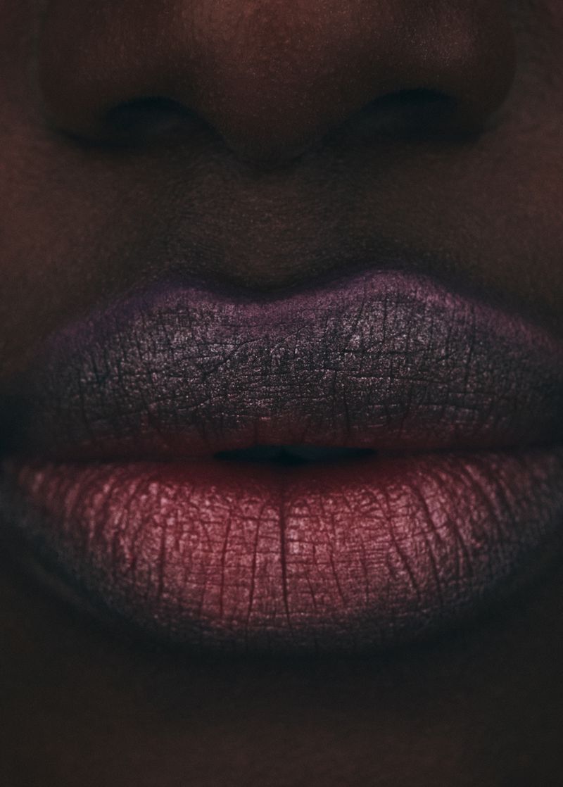 Close-up of an African-descent female face, displaying vibrant ombre lipstick in shades of red and purple, with dark skin.