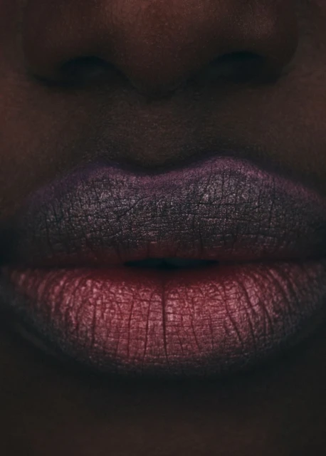 Close-up of an African-descent female face, displaying vibrant ombre lipstick in shades of red and purple, with dark skin.