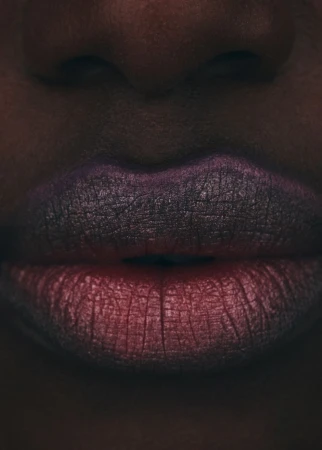 Close-up of an African-descent female face, displaying vibrant ombre lipstick in shades of red and purple, with dark skin.