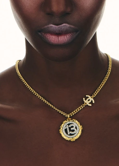 Close-up on a Black woman's face and chest with a golden Chanel pendant necklace with a diamond-studded CC logo.