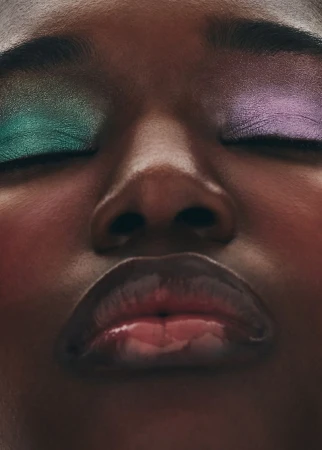 Close-up portrait of a Black model with metallic green and purple eyeshadow, closed eyes, and glossy lips for Grazia International.