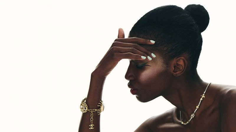 Close-up profile of a black woman wearing gold jewelry and a pendant necklace against a white background