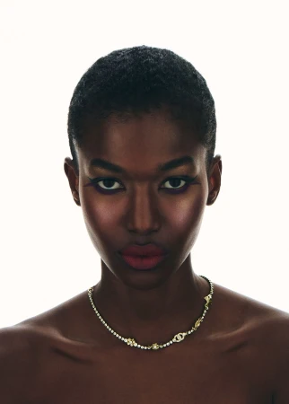 Portrait of a Black woman with short dark hair wearing a sparkling necklace against a bright white background