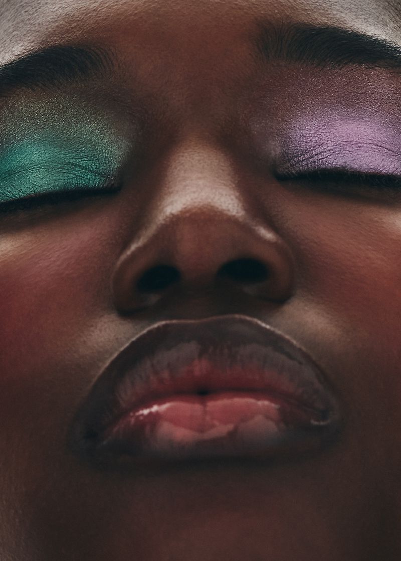 Close-up portrait of a Black model with metallic green and purple eyeshadow, closed eyes, and glossy lips for Grazia International.
