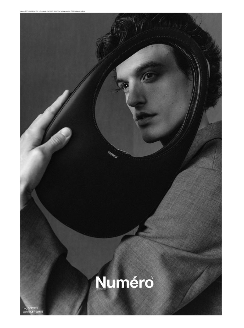 Black and white editorial portrait of a man looking through the oval cutout of a black leather handbag for Numero Netherlands