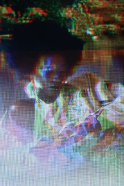 Abstract portrait of a person with dark hair and a patterned shirt, displayed with visual effects creating a colorful, distorted appearance.