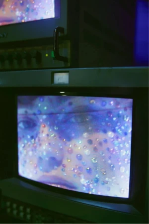 Television screens display a face covered in glitter in an indoor setting, with the focus on the screens and the displayed image.