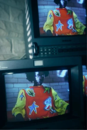 Monitors display a person in a colorful top against a brick wall. Retro technology, fashion, and urban setting merge in this image.