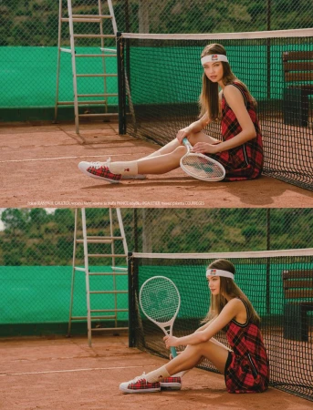 A young female model wearing a red plaid dress and white headband holds a tennis racket while seated on a clay tennis court.