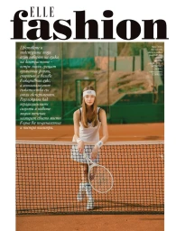 Model in white tennis attire leaning on a net at an outdoor clay tennis court
