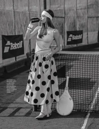 Black and white editorial fashion portrait of a female model on a tennis court drinking from a bottle with a polka dot skirt