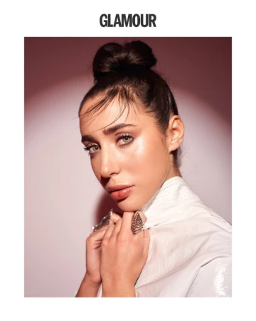 Glamour magazine portrait of an adult woman with a hair bun, wearing butterfly rings, a white jacket, and natural makeup.