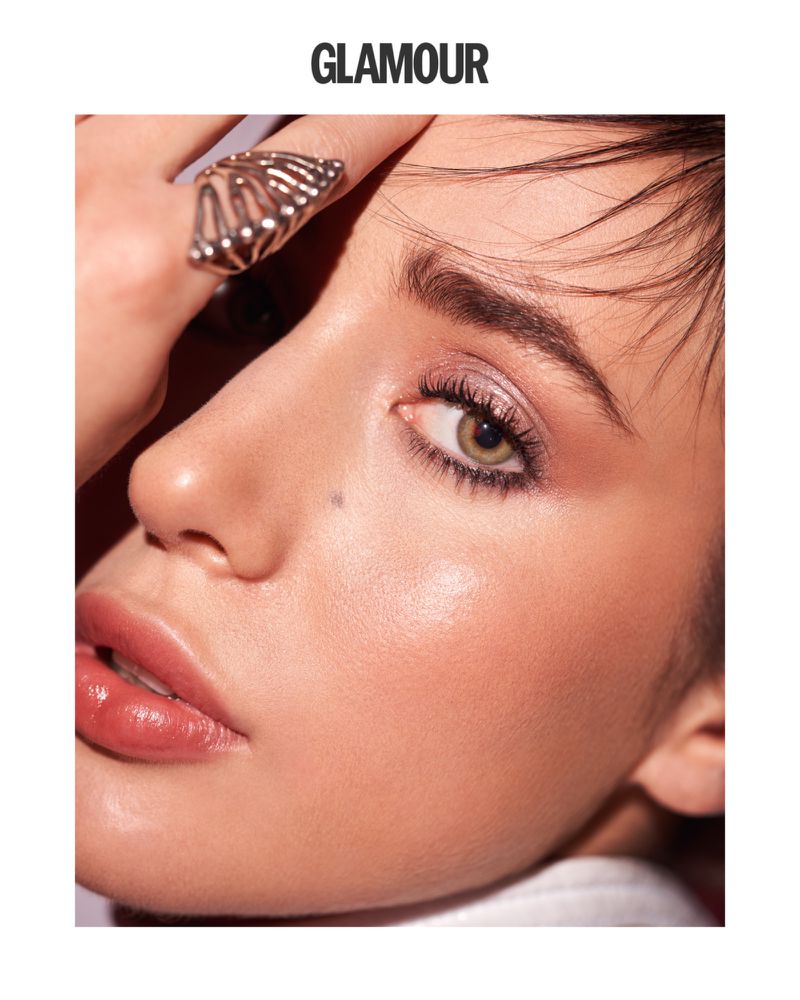 Close-up of a young adult female model showcasing makeup, featuring a butterfly ring on her hand and the word 'GLAMOUR' above.