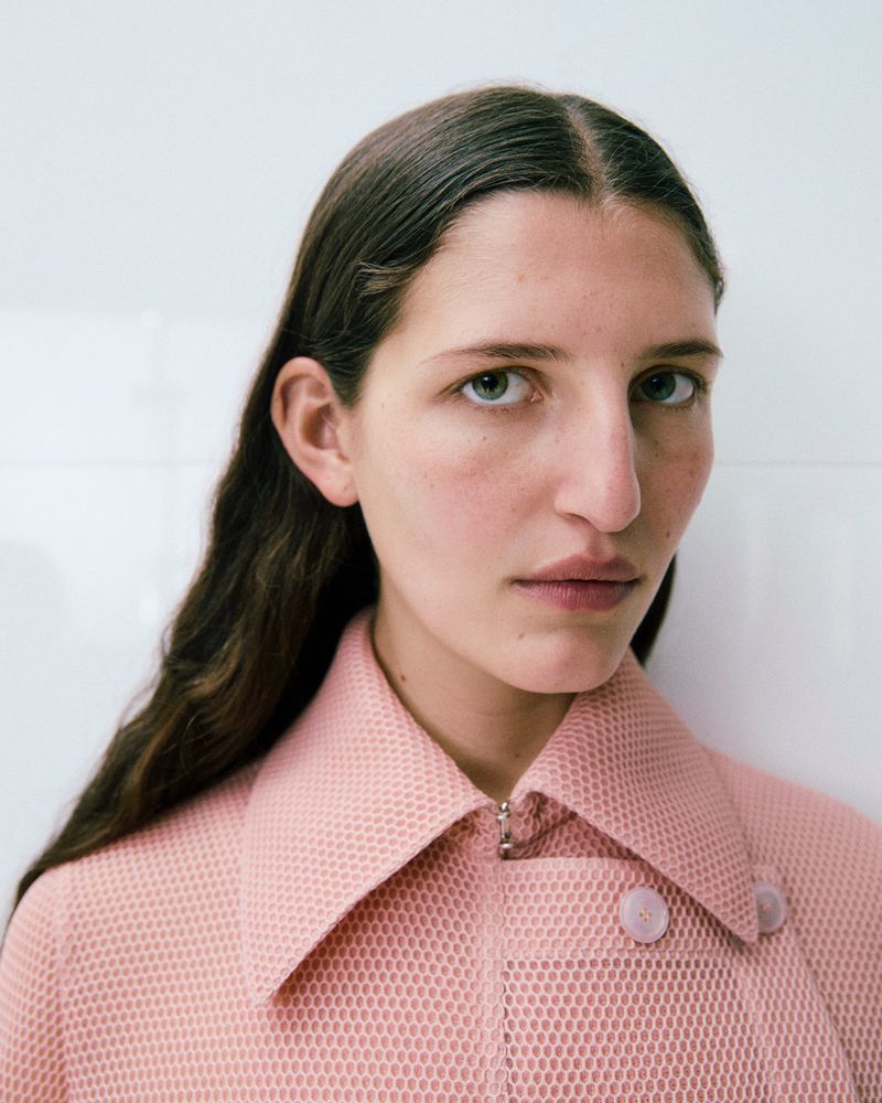 Portrait of a woman wearing a textured pink buttoned collared garment against a plain white background