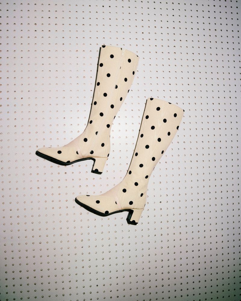 Polka dot boots. A pair of cream-colored, high-heeled boots with black polka dots, isolated against a white background with tiny black shapes.