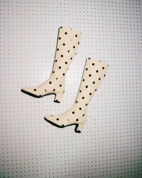 A pair of cream knee-high boots with black polka dots displayed against a white pegboard background.