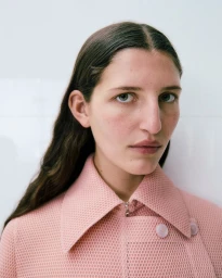 Portrait of a woman wearing a textured pink buttoned collared garment against a plain white background
