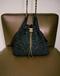 Chanel tweed bucket bag resting on an olive green leather chair in a minimalist editorial setting.