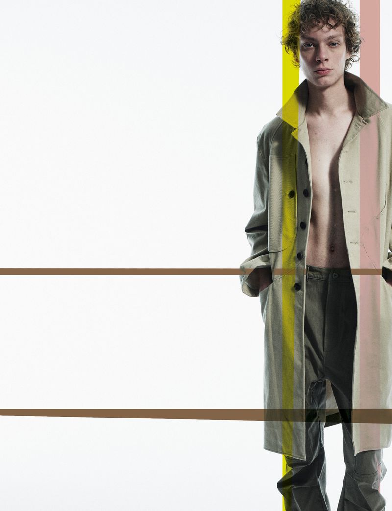 Fashionable young adult male poses in an open trench coat and pants against a white background with graphic colored stripes.