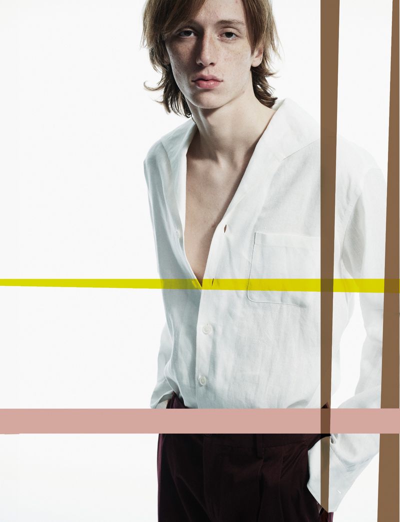 Studio portrait of a young adult male wearing a white button-down shirt and dark pants, posing against a bright white backdrop with graphic bars.