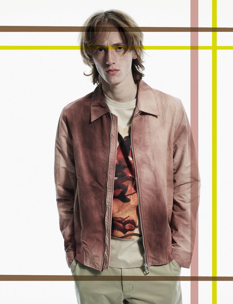 Adult male in an earth-toned bomber jacket and khaki pants posing against a white backdrop, with overlaid abstract geometric lines.