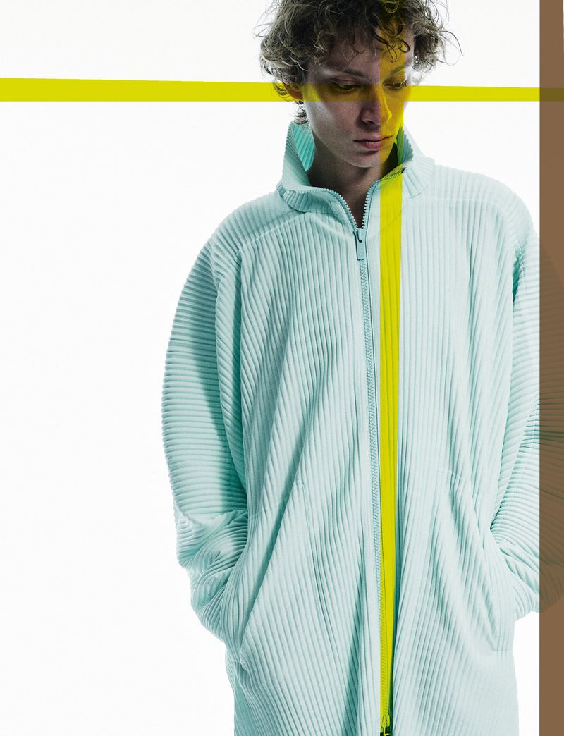 A person wearing a light turquoise, zip-up, ribbed jacket with a vertical neon yellow stripe, against a white background with yellow accents.