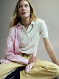 Model Reina Spoormaker wearing a white polo, pink shirt, and yellow trousers against a grey seamless background