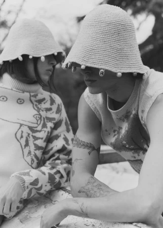 Two people wearing hats with beaded trim, one in patterned sweater, outdoor setting in black and white, showcasing textures and unique style.