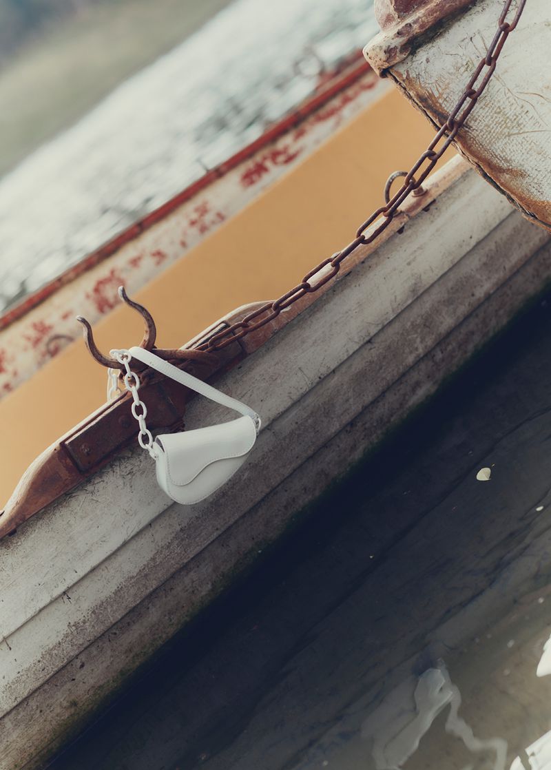 White purse with a chain strap hangs on the side of a weathered rowboat with yellow interior, partially submerged in dark water.