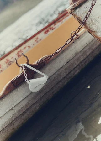 White purse with a chain strap hangs on the side of a weathered rowboat with yellow interior, partially submerged in dark water.