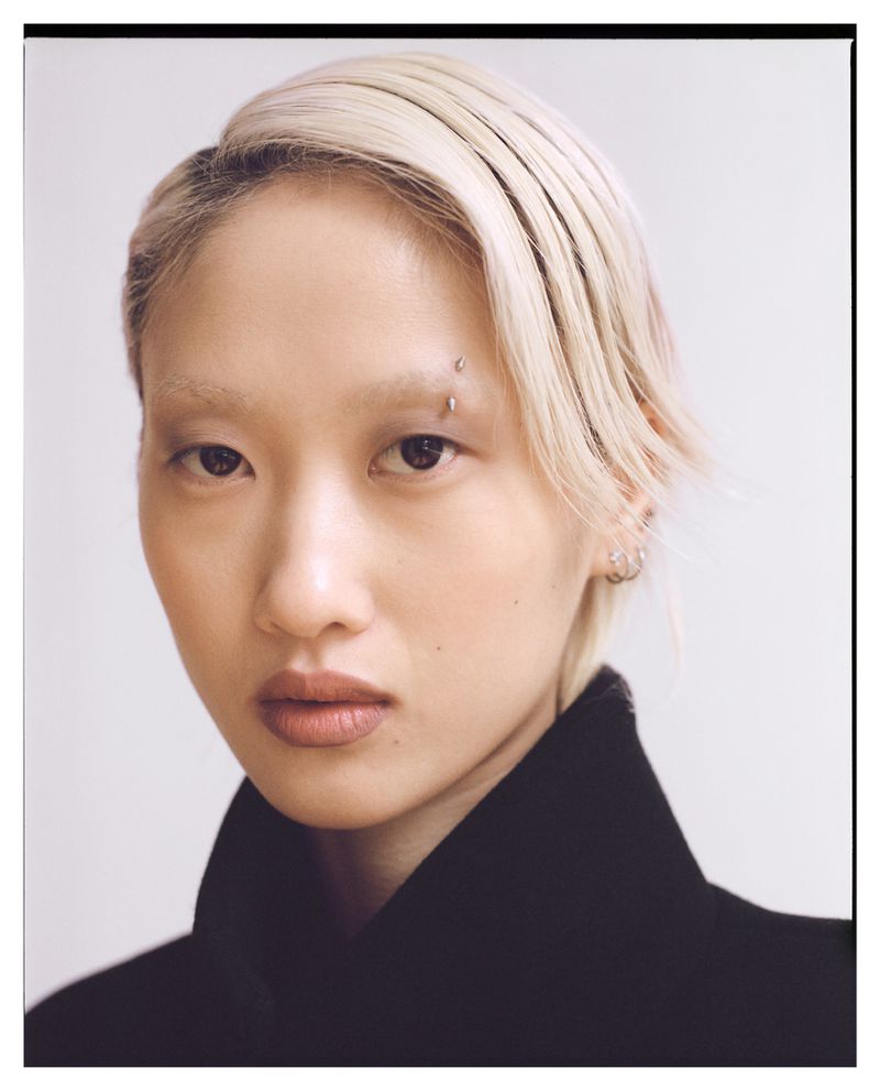 Close-up portrait of a young woman with dyed blonde hair and an eyebrow piercing against a white background, fashion, and beauty.