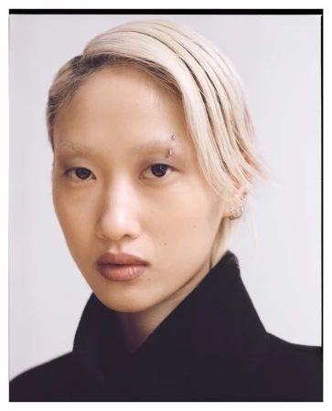 Close-up portrait of a young woman with dyed blonde hair and an eyebrow piercing against a white background, fashion, and beauty.