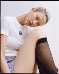 Model with blonde short hair wearing a white t-shirt, striped shorts, and black knee-high socks against a white studio background.