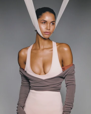 Portrait of a woman with tanned skin wearing a dress and long sleeves against a neutral gray background in a photo studio setting.