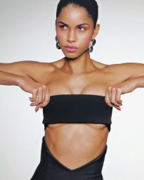 Model wearing a black strapless bandeau top and silver earrings against a white background for Allure Magazine.