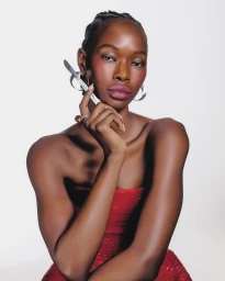 Black woman in a red strapless dress holding a surgical scalpel near her face against a white background