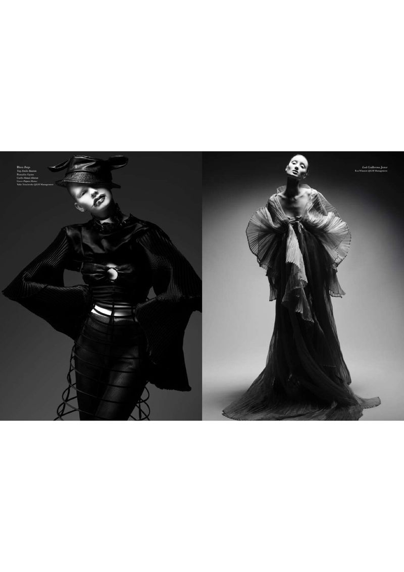 Black-and-white editorial fashion shot of two fashion models in dark clothing posing in a photo studio with dramatic lighting.