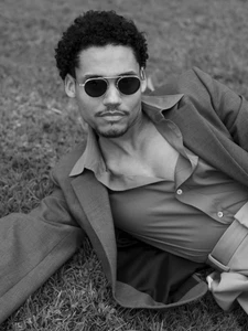 Man wearing sunglasses and a blazer lying on grass for Numero Netherlands, photographed by Tim Grupp.