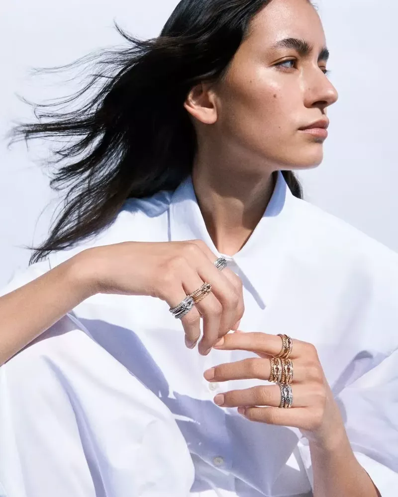 Close-up of a woman with dark hair modeling jewelry, showcasing multiple rings on her fingers against a bright white background.