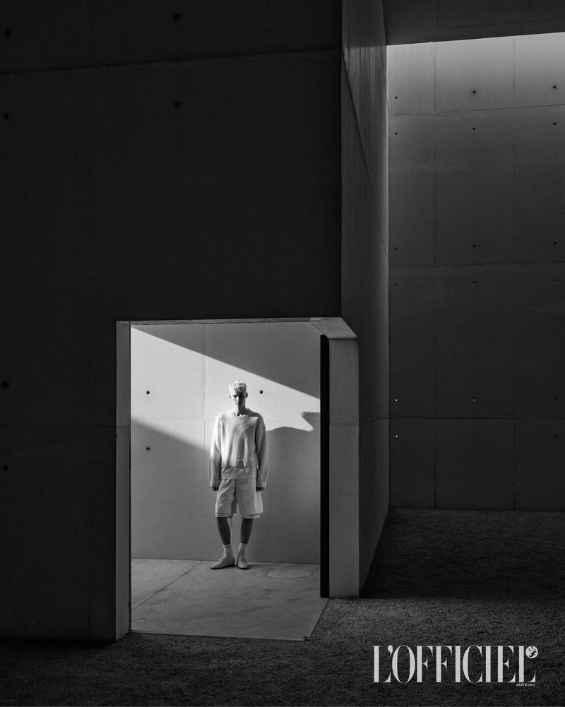 Monochrome fashion editorial portrait of a male model standing inside a stark architectural concrete doorway